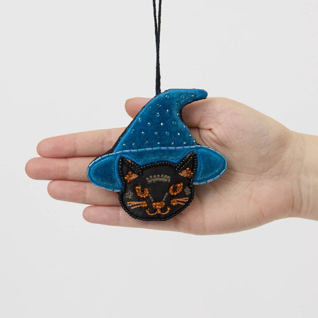 A double-sided handmade Black Cat Beaded Ornament featuring an intricately embroidered cat in a sparkling blue witch hat, with a playful “Boo” on the reverse.