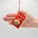 Miniature felt ornament shaped like a cookbook, hand-felted and embroidered with cooking-themed details including salt, pepper, vegetables, and a stovetop. Crafted from merino-blend wool with soft pages and a hanging string, this ornament measures approximately 2.5 inches tall. A cozy tribute to home cooking and culinary tradition. Held in a hand for scale reference.