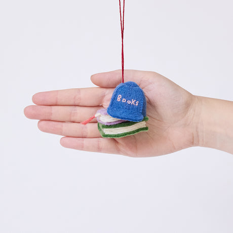 Craftspring’s Books Are Magic Hat with Books ornament held in front of a hand to show its size—handmade from sustainable wool with a whimsical blue hat and stacked books design, ethically crafted by artisans using sustainable wool.