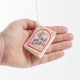 Hot pink felt ornament shaped like a small book, featuring delicately embroidered open pages. Inspired by the beloved Brooklyn bookstore Books Are Magic, this hand-felted wool ornament includes a hanging string and measures approximately 2.5 inches tall. A colorful tribute to the joy of reading and storytelling.  Held in a hand for scale reference.
