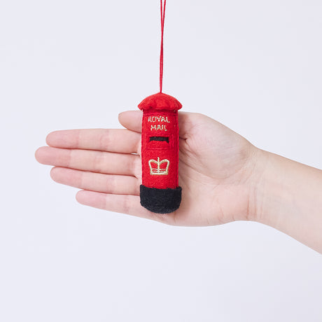 Craftspring’s British Post Box ornament held in front of a hand to show its size—handmade from sustainable wool with a classic red design and gold embroidered details, ethically crafted by artisans using sustainable wool.