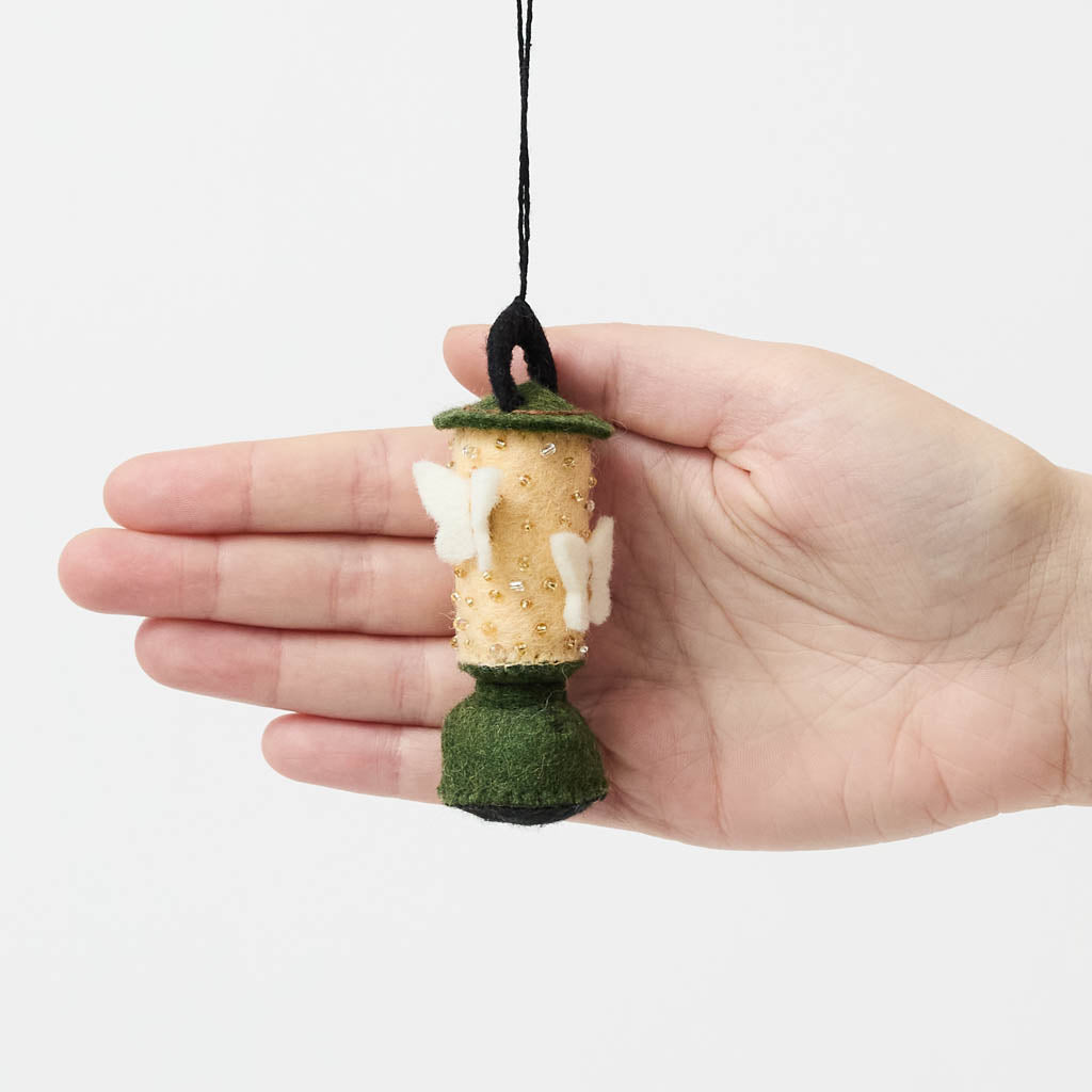 Handcrafted from natural wool felt, this charming vintage-inspired lantern features soft ivory tones accented with shimmering golden beadwork that mimics the gentle glow of lantern light. Delicate felt moths flutter around the lantern, adding a whimsical touch that captures the quiet magic of nature at dusk. Rich forest green details complete the design, making it a timeless keepsake for campers, hikers, glampers, and outdoor dreamers alike.