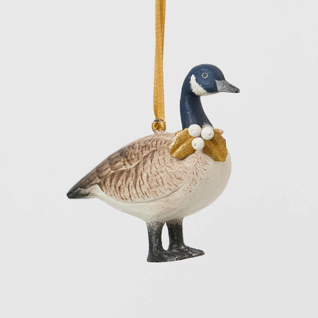 A vintage-inspired Canada Goose Resin Ornament, hand-painted in the Philippines with classic black-and-white markings, a golden metal holly necklace, and satin hanging ribbon.