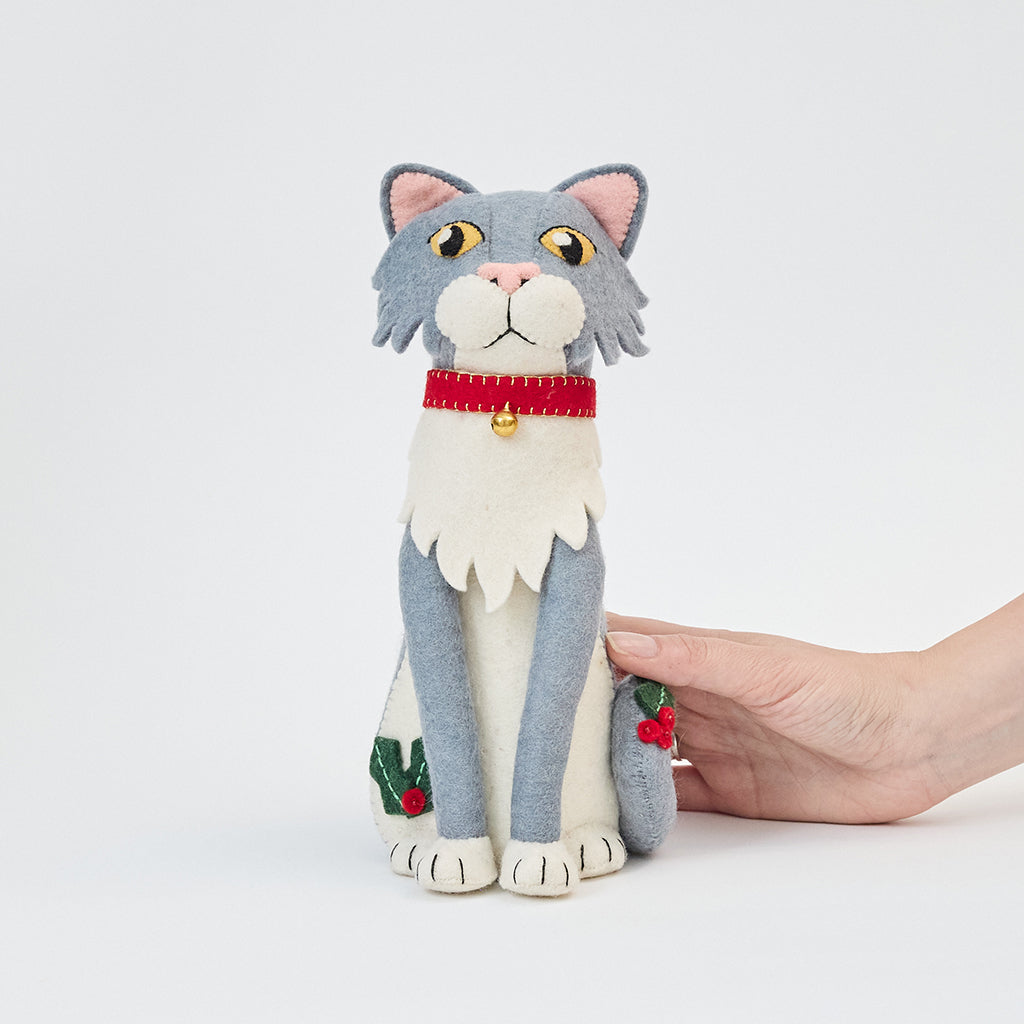 Handmade felt Gray Cat Tree Topper from Craftspring held in hand to show size—featuring a red collar with a bell and festive holly, showcasing heirloom-quality holiday decor, ethically crafted by artisans using sustainable wool.