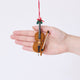 Craftspring’s Cello Ornament displayed in front of a hand to show its size — handmade from sustainable wool with a bow, holly, and detailed embroidery, ethically crafted by artisans using sustainable wool.