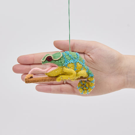 Craftspring’s Chameleon ornament held in front of a hand to show its size—handmade from sustainable wool with beaded details, a curled tail, and a long tongue catching a bug, ethically crafted by artisans using sustainable wool.