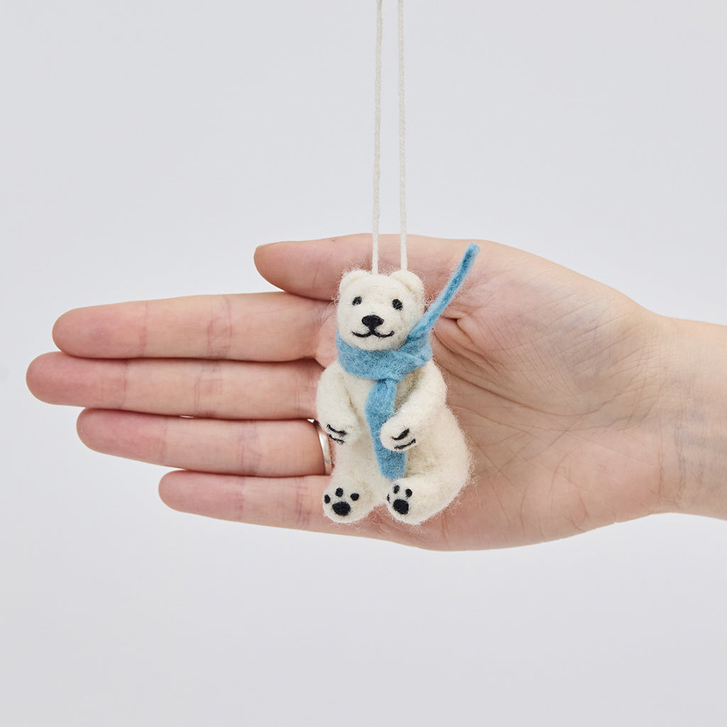 Handmade needle-felted Chilly Polar Bear ornament from Craftspring held in front of a hand to show its size—featuring a cozy blue scarf and detailed needle felting, ethically crafted by artisans using sustainable wool.