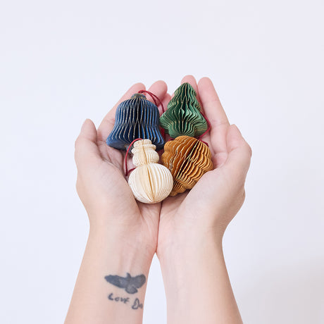 Craftspring’s Classic Christmas Honeycomb Paper Mini Ornaments — Set of 4, held in hand, showing the snowman, bell, pinecone, and tree with gold sparkly edges, handmade by artisans from recycled cotton waste.
