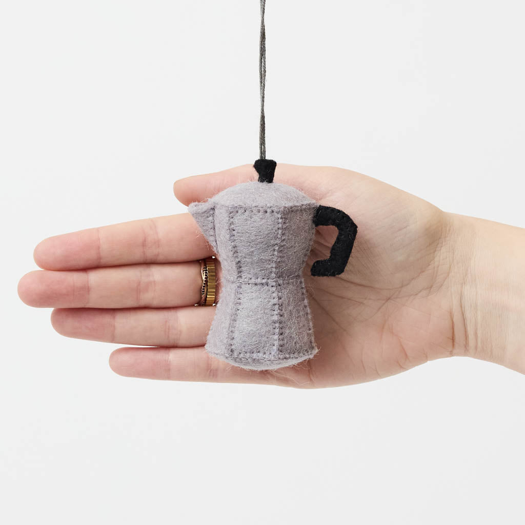 Handcrafted from natural wool felt, this charming ornament is inspired by the classic stovetop camping percolator—a beloved companion for generations of campers, hikers, RV travelers, and cabin lovers. Its timeless silhouette, soft neutral tones, and handcrafted stitching evoke memories of peaceful mornings surrounded by towering pines, fresh mountain air, and the sounds of nature waking up.
