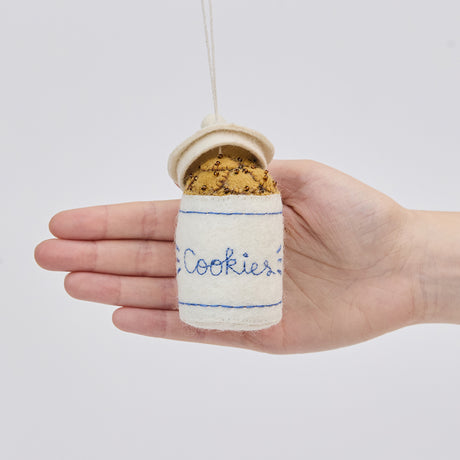 Handmade felt Cookie Jar ornament from Craftspring held in front of a hand to show its size—featuring detailed embroidery and beading of chocolate chip cookies in a classic jar, ethically crafted by artisans using sustainable wool.