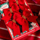 A set of four red felt bows with beaded detailing, packaged in a box with a Christmas-themed design.