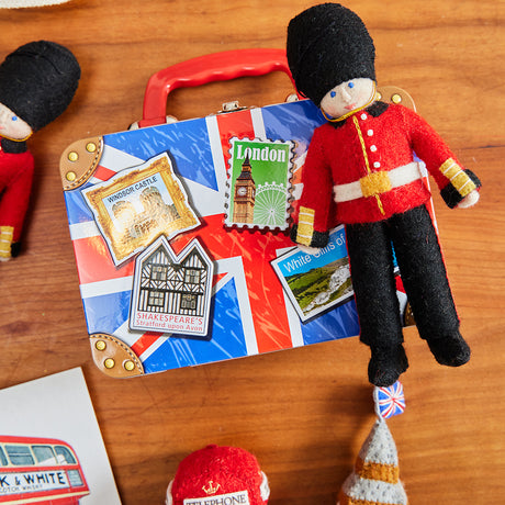 Queen’s Guard felt ornament wearing red coat and black bearskin hat, inspired by Buckingham Palace guards. Handmade wool Christmas ornament celebrating British tradition. Fair trade and ready to hang.