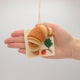 Hand-felted ornament of a golden-brown croissant resting on a pink felt napkin embroidered with a strawberry. Crafted from merino-blend wool with detailed stitching to mimic flaky layers, this ornament includes a hanging string and measures approximately 3.75 inches wide. A charming tribute to French pastry and cozy café mornings.