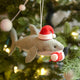 Craftspring’s Jolly Santa Shark with Santa Leg Ornament — a playful shark wearing a Santa hat and holding Santa’s leg in its mouth, with beaded and embroidered holiday details — displayed on a glowing Christmas tree, bringing humorous, joy-filled warmth to festive decorating and holiday gifting, ethically crafted by artisans using sustainable wool.