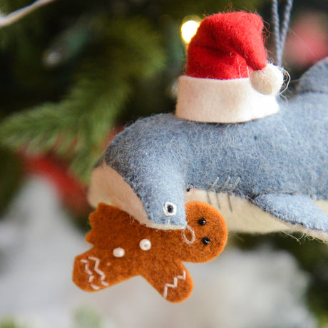 Craftspring’s Take a Bite Out of Christmas Hammerhead Ornament — a festive hammerhead shark wearing a Santa hat and munching a gingerbread man, detailed with beaded and embroidered holiday accents — displayed on a glowing Christmas tree, adding humorous charm, heirloom-quality warmth, and gift-ready Christmas cheer, ethically crafted by artisans using sustainable wool.