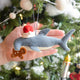 Craftspring’s Take a Bite Out of Christmas Hammerhead Ornament displayed in front of a hand to show its size — featuring a Santa hat and a gingerbread man between its sharky jaws with beaded and embroidered details — a whimsical holiday piece perfect for joyful Christmas gifting, ethically crafted by artisans using sustainable wool.