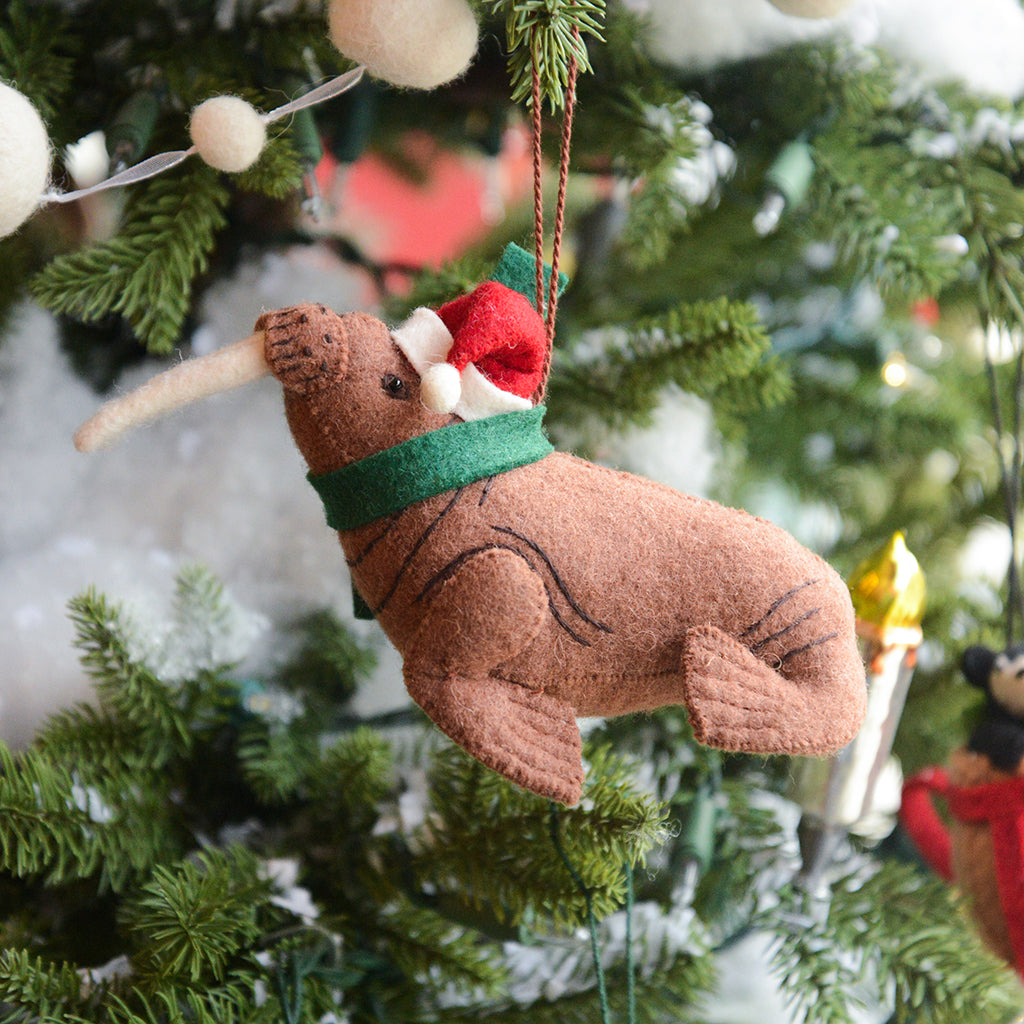 Craftspring’s Santa Walrus Ornament — a charming walrus wearing a Santa hat and a cozy holiday scarf with embroidered details — displayed on a glowing Christmas tree, bringing whimsical warmth, festive delight, and gift-ready Christmas cheer, ethically crafted by artisans using sustainable wool.
