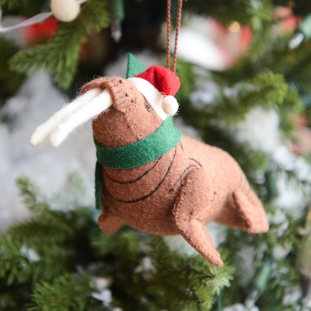 Craftspring’s Santa Walrus Ornament — a charming walrus wearing a Santa hat and a cozy holiday scarf with embroidered details — displayed on a glowing Christmas tree, bringing whimsical warmth, festive delight, and gift-ready Christmas cheer, ethically crafted by artisans using sustainable wool.