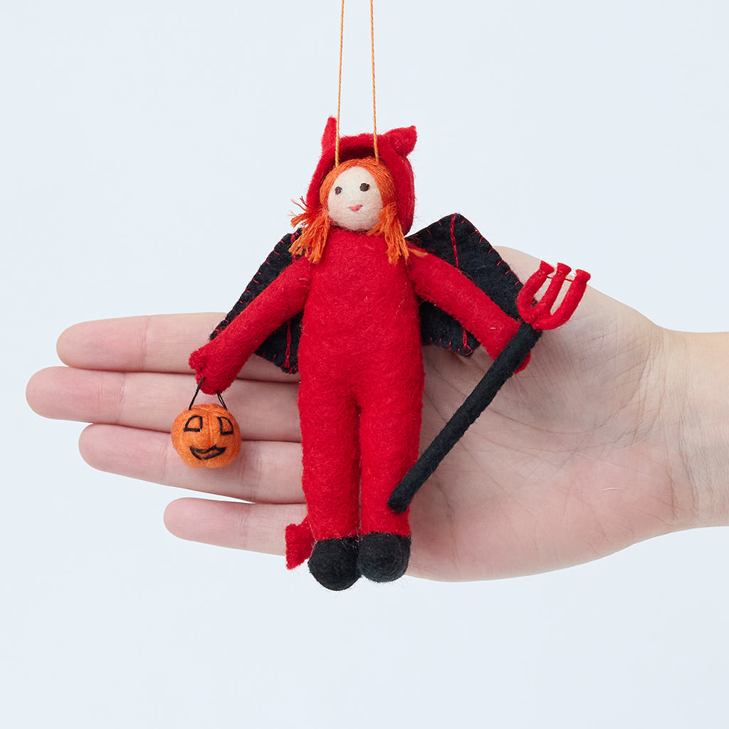 Craftspring’s Devil Trick-Or-Treater Ornament displayed in front of a hand to show its size—handmade felt girl in a devil costume, heirloom-quality Halloween decor, ethically handcrafted by artisans using sustainable wool.