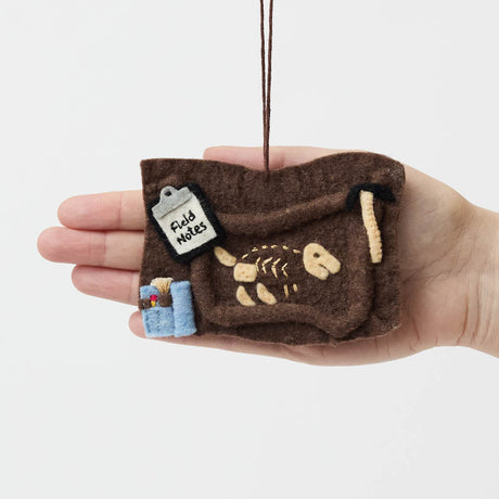 Unearth a piece of prehistoric wonder with our Felt Dinosaur Bones Ornament. Carefully handcrafted by skilled artisans using sustainable wool felt, this charming ornament features an excavation scene complete with partially uncovered dinosaur fossils, excavation tools, field notes, and scientific equipment.