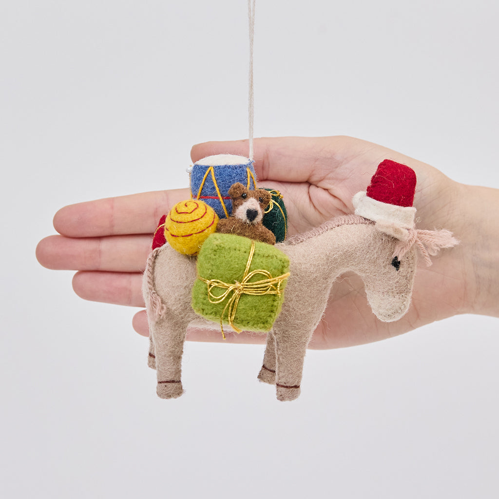 Handmade felt Donkey with Gifts ornament from Craftspring held in front of a hand to show its size—featuring a Santa hat and detailed toys on its back, showcasing heirloom-quality Christmas decor, ethically crafted by artisans using sustainable wool.