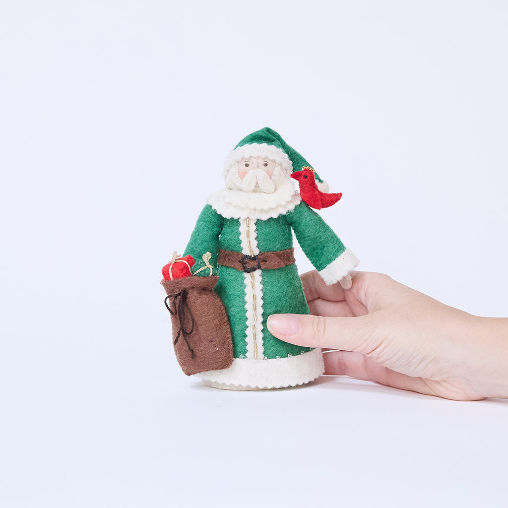 Craftspring’s Emerald Santa Mini Tree Topper held in hand to show its size — felt Santa in a green cloak with beaded details, holding a sack of presents and a bird on his shoulder, a charming heirloom-quality piece for holiday gifting — ethically crafted by artisans using sustainable wool.