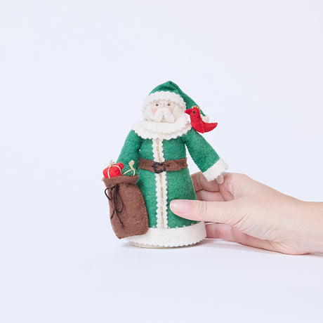 Craftspring’s Emerald Santa Mini Tree Topper held in hand to show its size — felt Santa in a green cloak with beaded details, holding a sack of presents and a bird on his shoulder, a charming heirloom-quality piece for holiday gifting — ethically crafted by artisans using sustainable wool.