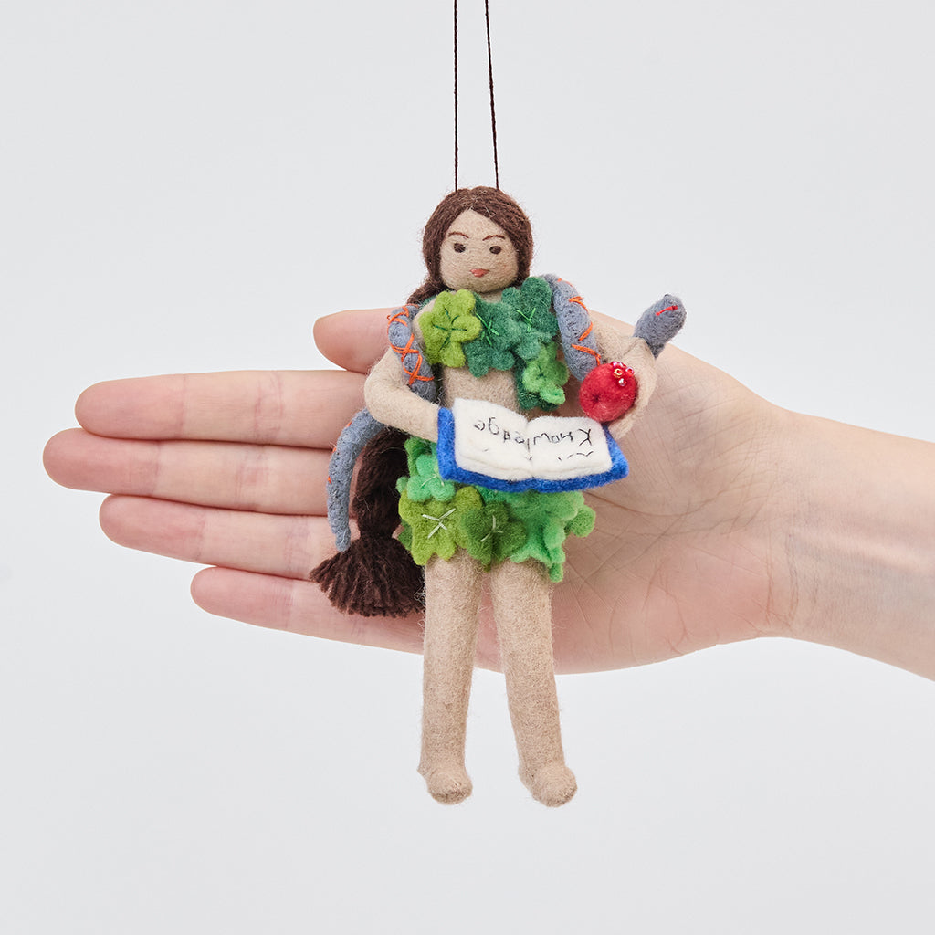 Craftspring’s Eve ornament held in front of a hand to show its size—handmade from sustainable wool with Eve holding a book of knowledge and an apple, wrapped in leaves with a serpent around her shoulders, ethically crafted by artisans using sustainable wool.