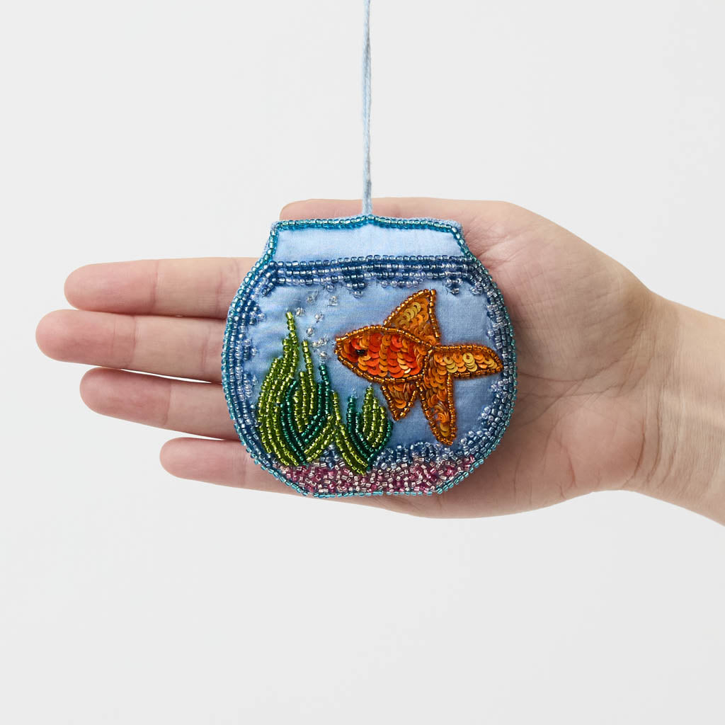 Make a splash with our whimsical Fishbowl Beaded Ornament! 🐠✨ This beautifully handcrafted ornament captures the charm of a beloved goldfish swimming peacefully through its miniature underwater world. Featuring a shimmering sequined goldfish, vibrant hand-beaded aquatic plants, and a sparkling fishbowl outlined with delicate glass beads, every detail is carefully stitched by hand to create a dazzling keepsake.