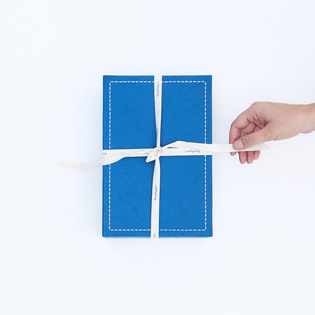 Hand opening the twill ribbon on a Craftspring blue gift box—high-quality, artisan-crafted packaging that captures the warmth of Christmas and holiday giving.