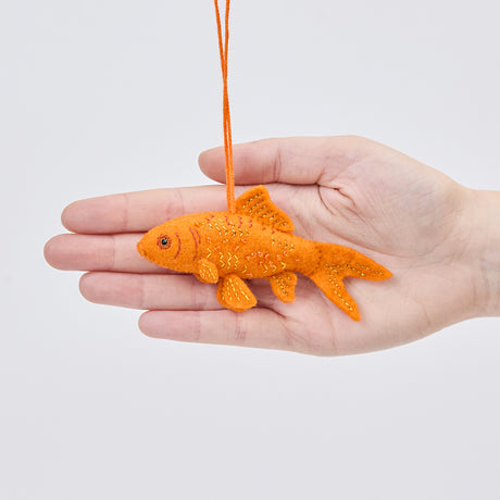 Handmade felt Goldfish ornament from Craftspring held in front of a hand to show its size—featuring intricate beaded and embroidered details on orange felt, ethically crafted by artisans using sustainable wool.