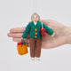 Handmade felt Grandma ornament from Craftspring held in front of a hand to show its size—featuring intricate beaded and embroidered details on a holiday sweater, a designer purse, and a shopping bag full of presents, ethically crafted by artisans using sustainable wool.