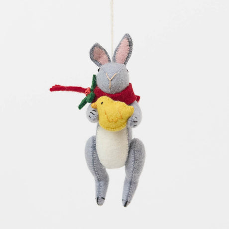 Our Gray Holiday Bunny with Chick Ornament captures a heartwarming moment of gentle friendship. Wrapped in a cozy red scarf adorned with festive holly leaves and tiny red berries, this sweet gray bunny lovingly cradles a fluffy yellow chick, creating a scene that's full of warmth, comfort, and Christmas cheer.