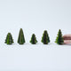 Craftspring’s Green Honeycomb Paper Mini Trees displayed in front of a hand to show scale — Set of 5 with several shades of green, gold sparkle on the edges, and varying shapes, handmade by artisans from recycled cotton waste.