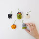 A handmade felt Halloween Mini Ornaments Set featuring five tiny spooky-season favorites: a black cat, candy-filled monster bucket, ghost, jack-o’-lantern, and RIP tombstone.