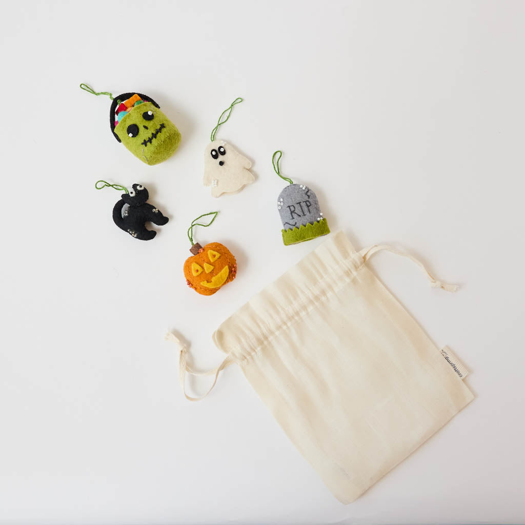 A handmade felt Halloween Mini Ornaments Set featuring five tiny spooky-season favorites: a black cat, candy-filled monster bucket, ghost, jack-o’-lantern, and RIP tombstone.