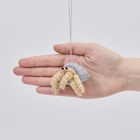 Handmade felt Hermit Crab ornament from Craftspring held in front of a hand to show its size—featuring intricate beaded and embroidered details on the shell and legs, ethically crafted by artisans using sustainable wool.