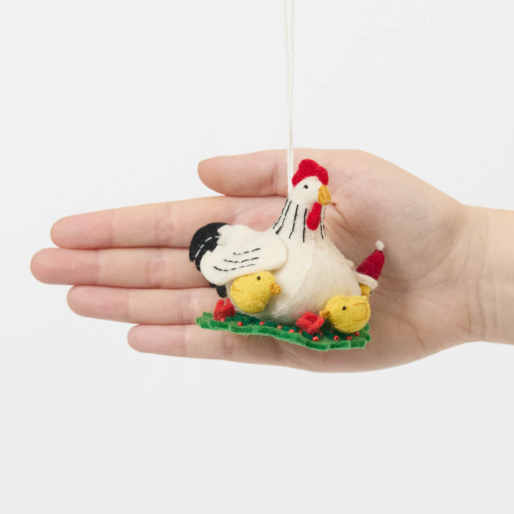 Gathered together on a festive green wreath our Holiday Hen with Chicks Ornament is a sweet celebration of family, nurturing, and holiday togetherness. A proud mother hen watches over her fluffy yellow chicks, while one festive little chick sports a tiny red Santa hat, adding an extra dash of Christmas cheer. 