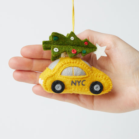 Craftspring’s Holiday Taxi Ornament from the Christmas in the City NYC Ornaments Bundle displayed in front of hand to show its size — felt taxi with a Christmas tree on top, a charming heirloom-quality piece for Christmas gifting — ethically crafted by artisans using sustainable wool.