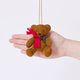 Craftspring’s Holiday Teddy Bear Ornament displayed in front of a hand to show its size — felt vintage-style teddy bear wearing a red scarf with holly, a charming heirloom-quality piece for Christmas gifting — ethically crafted by artisans using sustainable wool.