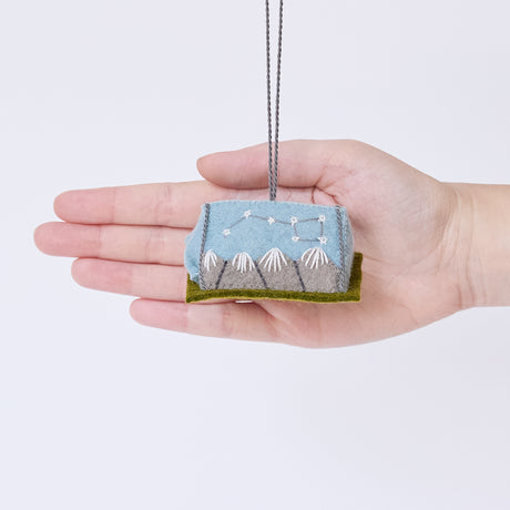 Craftspring’s Home Under the Stars Tent ornament held in front of a hand to show its size—handmade from sustainable wool with applique and embroidered mountains, the Big Dipper on the side, and a mini felt mattress inside the tent, ethically crafted by artisans using sustainable wool.