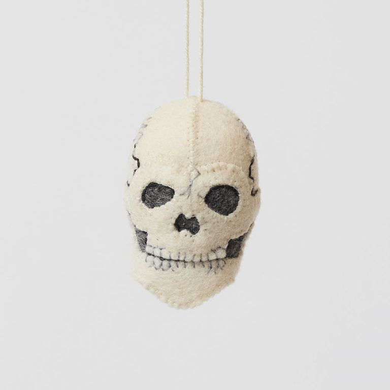 A handmade felted and embroidered Human Skull Ornament featuring embroidered bone, teeth, and crack details for a delightfully spooky addition to Halloween décor.