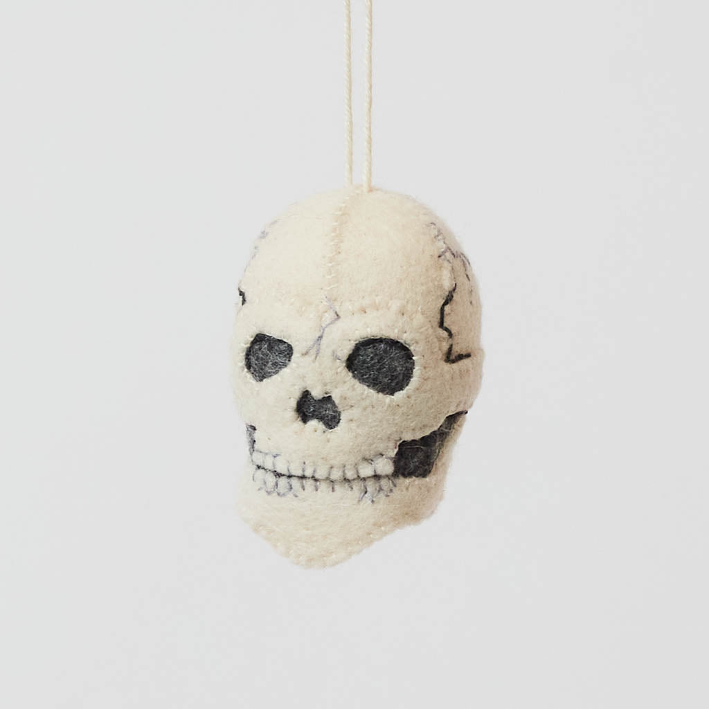 A handmade felted and embroidered Human Skull Ornament featuring embroidered bone, teeth, and crack details for a delightfully spooky addition to Halloween décor.
