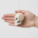 A handmade felted and embroidered Human Skull Ornament featuring embroidered bone, teeth, and crack details for a delightfully spooky addition to Halloween décor.