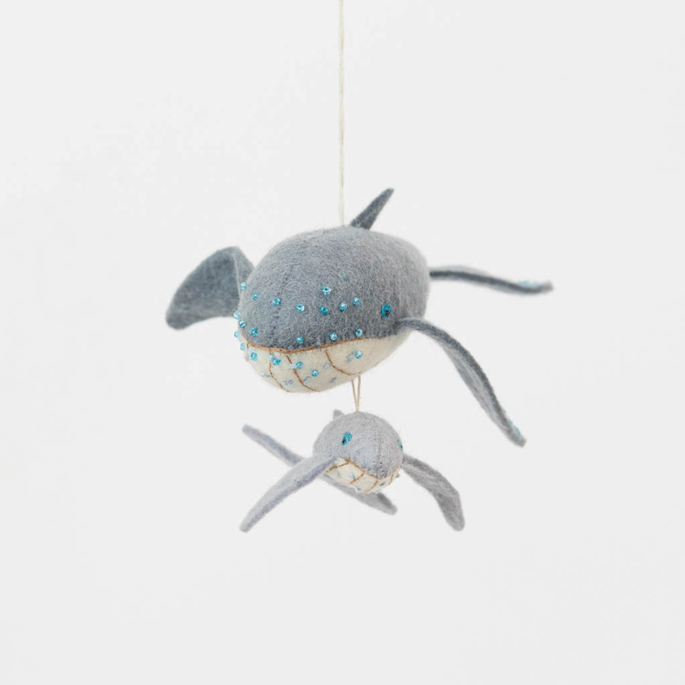Graceful, gentle, and full of wonder, our Humpback Whale with Baby Ornament captures one of nature’s most touching sights—a mother whale guiding her calf through the open sea. Handcrafted from soft felted wool and accented with shimmering blue beadwork, this beautiful ornament celebrates the deep connection between parent and child while honoring the majestic marine life that frequents Maine’s coastal waters.