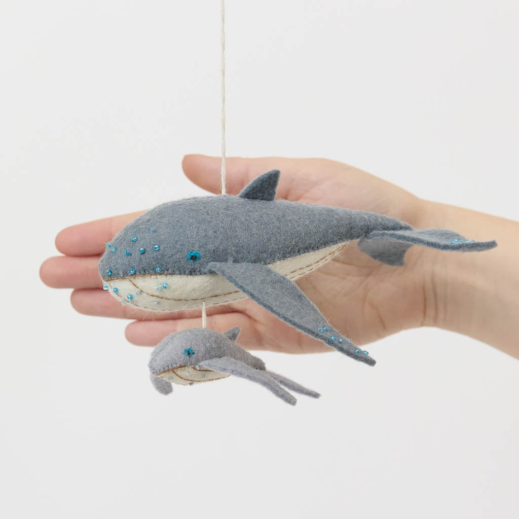 Graceful, gentle, and full of wonder, our Humpback Whale with Baby Ornament captures one of nature’s most touching sights—a mother whale guiding her calf through the open sea. Handcrafted from soft felted wool and accented with shimmering blue beadwork, this beautiful ornament celebrates the deep connection between parent and child while honoring the majestic marine life that frequents Maine’s coastal waters.