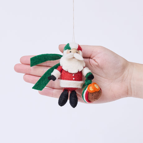 Craftspring’s Italian Santa ornament held in front of a hand to show its size—handmade from sustainable wool with a cute Santa holding a panettone and wearing a helmet in Italian flag colors, ethically crafted by artisans using sustainable wool.