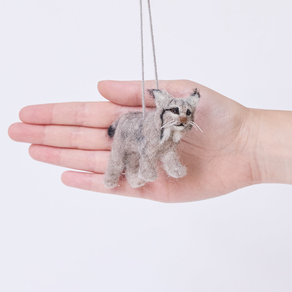 Craftspring’s Lynx ornament held in front of a hand to show its size — handmade from sustainable wool with lifelike details, including whiskers and ear tufts, ethically crafted by artisans.