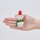Handmade felt Little Drop Polar Bear ornament from Craftspring held in front of a hand to show its size—featuring a Santa hat and green scarf with detailed stitching, ethically crafted by artisans using sustainable wool.