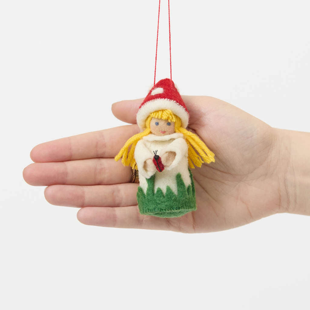 A magical little child of the forest, bringing good fortune, woodland wonder, and a sprinkle of fairy-tale enchantment into your home all year round! This sweet little red Amanita mushroom girl ornaments features a bright red felted mushroom cap, dotted with delicate white spots, and a skirt hemmed with felted green grasses. 
